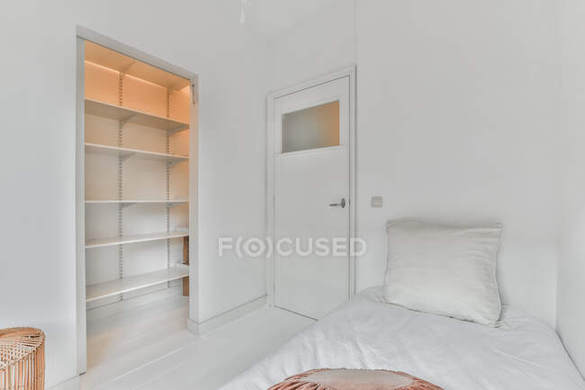 Интерьер светлой спальни с мягкой кроватью и пустыми полками в современной квартире — стоковое фото