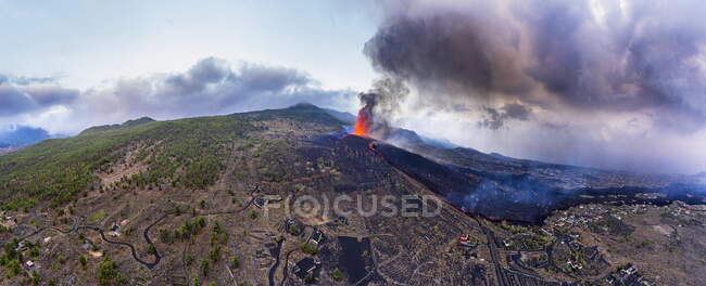 Vista aérea de la lava caliente y el magma saliendo del cráter con columnas de humo cerca de las casas de la ciudad. Cumbre Vieja erupción volcánica en La Palma Islas Canarias, España, 2021 - foto de stock