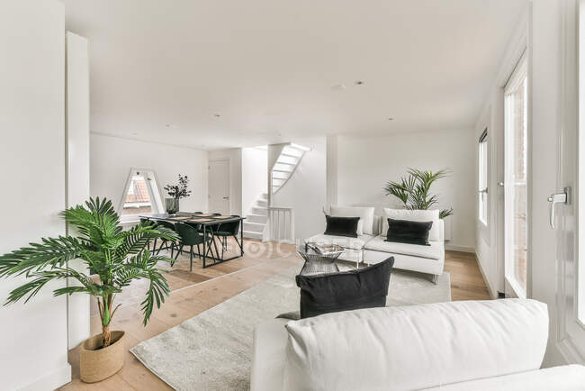 Інтер'єр сучасного двоповерхового будинку з білим диваном з подушками на килимі та їдальні — стокове фото