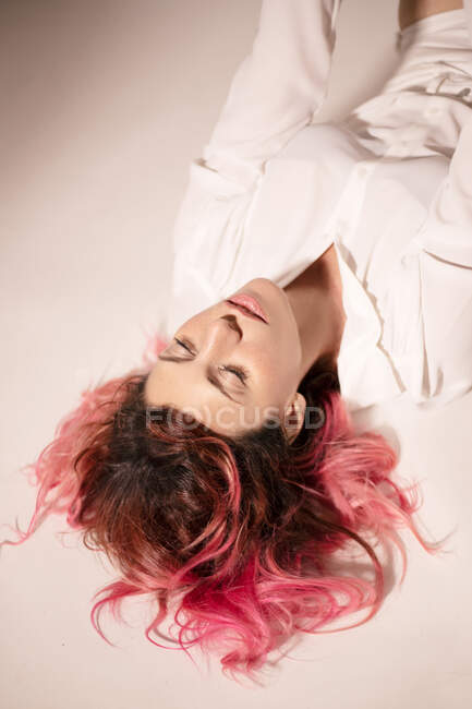 From above of tranquil female with pink hair lying with closed eyes on floor in light room — Stock Photo