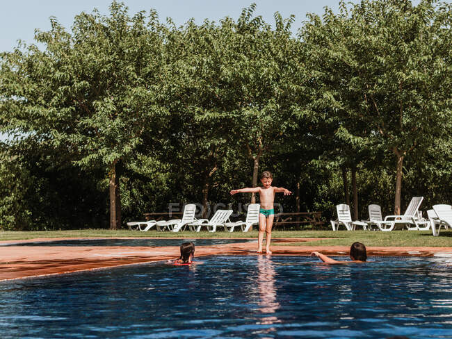 Little boy walking into water of swimming pool while entertaining with friends during summer weekend on sunny day — Stock Photo