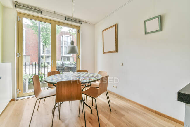 Round dining table with chairs near glass balcony doors in modern apartment decorated with frames on wall — Stock Photo