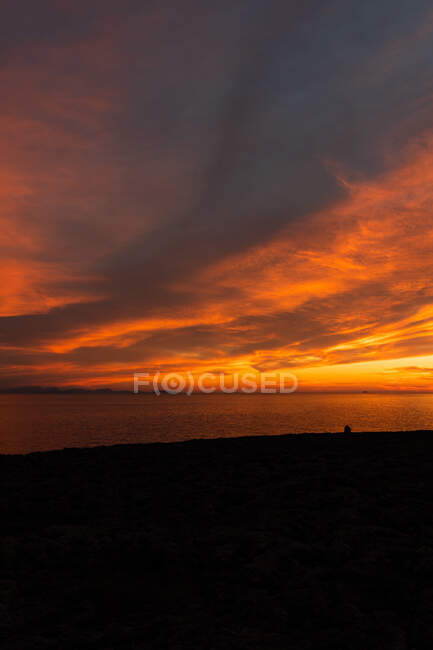 Spettacolare vista della silhouette del viaggiatore contemplando oceano dalla spiaggia sotto cielo nuvoloso colorato al tramonto — Foto stock