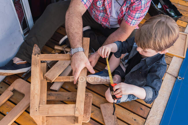 Сверху небритый зрелый папа с внимательным мальчиком, который измеряет деревянные блоки лентой, проводя время на размытом фоне. — стоковое фото