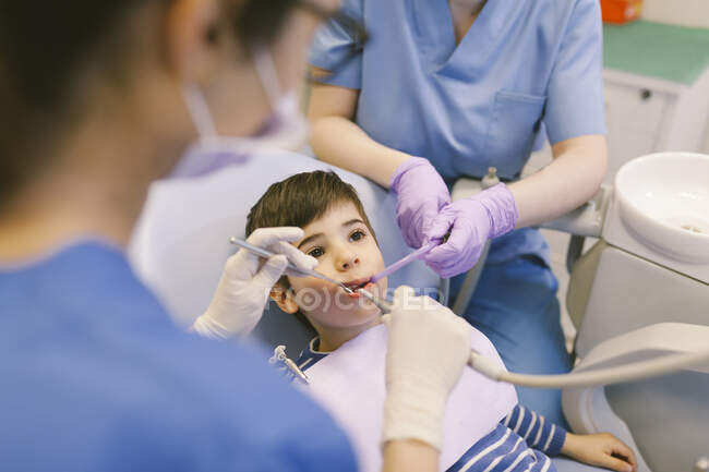 Angle élevé de dentiste de culture et assistant traitant les dents du garçon pendant la procédure dans la clinique de dentisterie — Photo de stock
