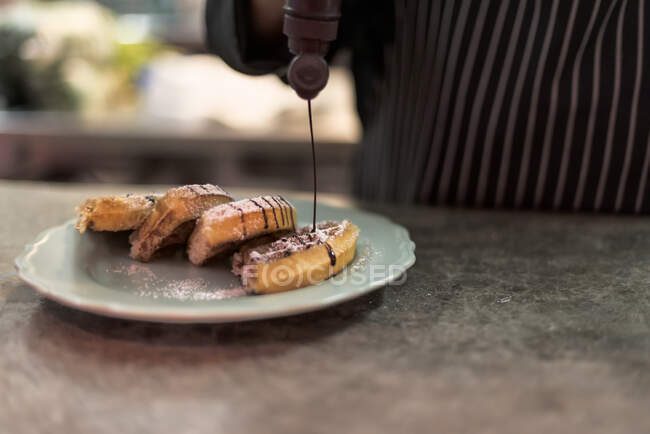 Ernte bis zur Unkenntlichkeit männlicher Koch schmückt köstliche Wiener Waffeln mit Schokoladensoße aus der Flasche in Restaurantküche — Stockfoto