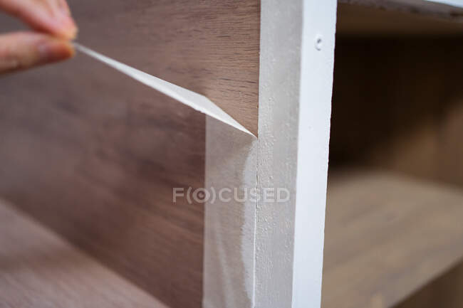 Recadrage anonyme femelle collage ruban adhésif blanc sur l'escalier pendant le processus de rénovation dans la maison — Photo de stock