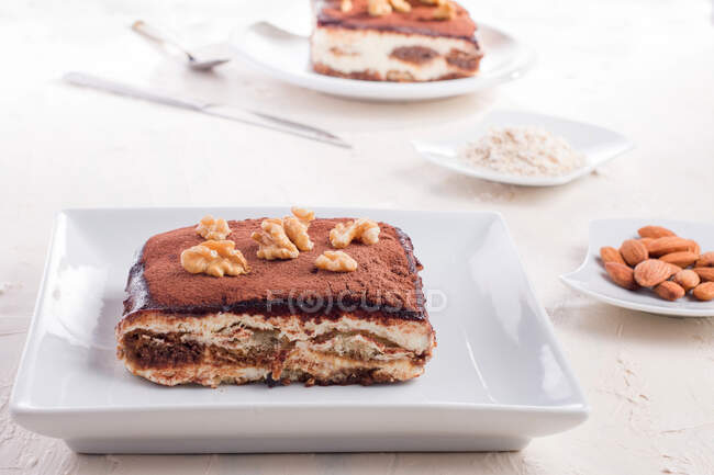 Высокий угол вкусного десерта тирамису, украшенного орехами, подаваемыми на белом столе — стоковое фото