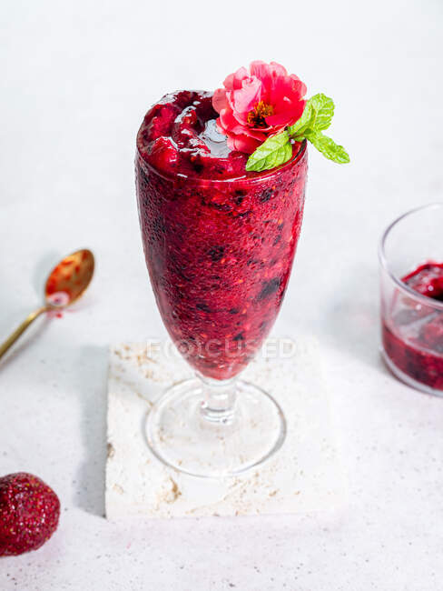 High angle of glass with sweet berry smoothie garnished with flower served on white background — Stock Photo