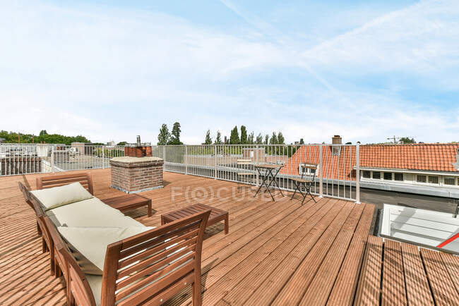 Стільці і диван розміщені біля дерев'яного столу на обгородженому балконі житлового передмістя району вдень — стокове фото