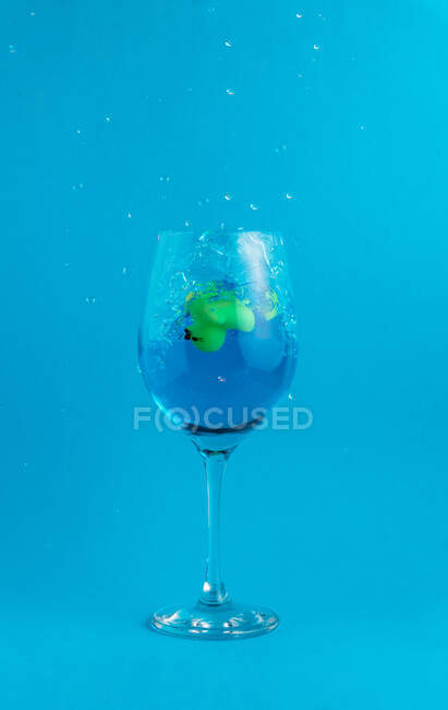 Lindo juguete de patito de goma colocado dentro de vidrio con agua sobre fondo azul brillante - foto de stock