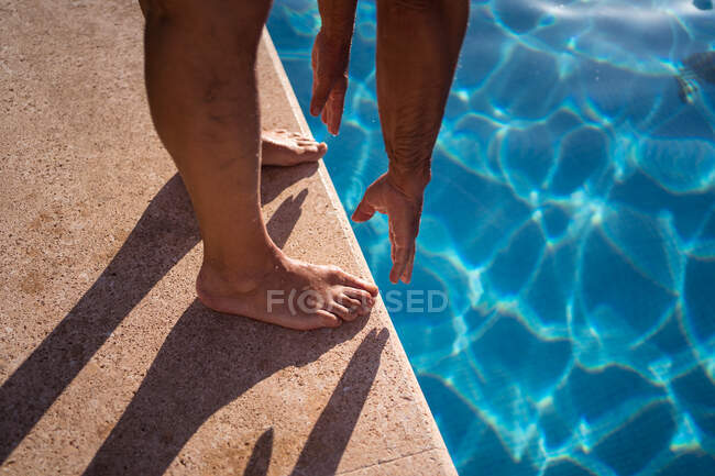 High angle of crop anonymous barefoot person stretching forward while standing on poolside edge near clean water — Stock Photo