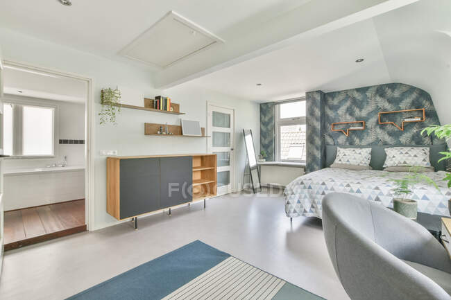 Weiches Bett mit weißer Bettwäsche in der Nähe des Arbeitsplatzes in einem geräumigen hellen Schlafzimmer in der Wohnung — Stockfoto