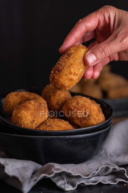 Crop unrecognizable person demonstrating yummy deep fried croquette on black background — Stock Photo