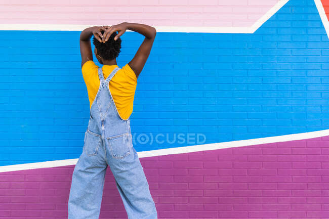 Back view of unrecognizable young African American female on overall standing on colorful bright wall — Stock Photo