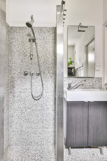 Bagno contemporaneo interno con cabina doccia a parete in ceramica grigia contro lavabo sotto specchio in casa luce — Foto stock