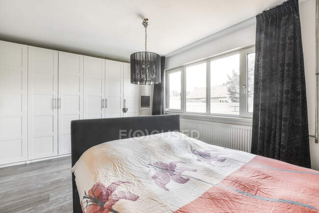 Удобная кровать с одеялом, размещенная в просторной современной спальне в квартире, оформленной в минимальном стиле — стоковое фото