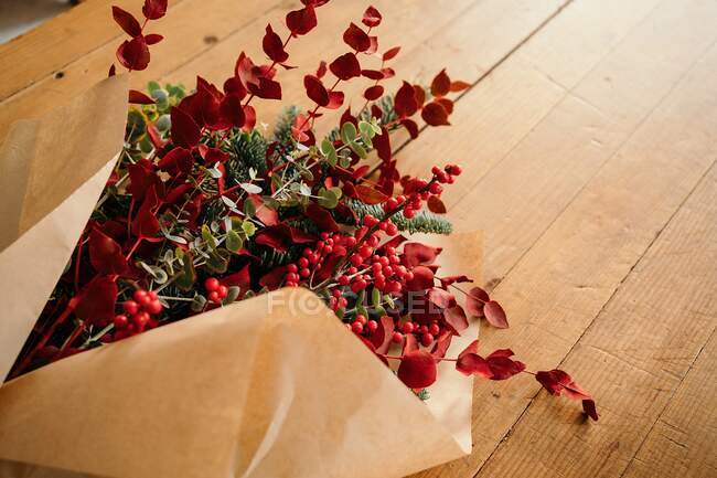 Dall'alto di bouquet di Natale decorativo elegante festivo con ramoscelli di eucalipto e rami rossi lucenti con bacche messe su tavolo di legno in camera — Foto stock