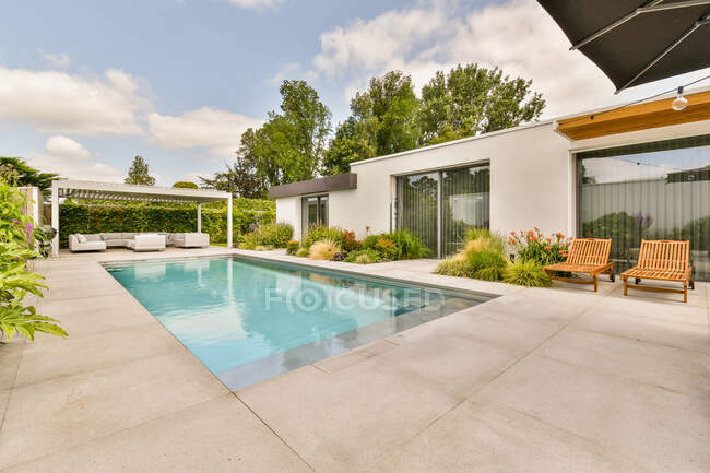 Cantiere di costosa villa moderna con piscina e zona lounge con comodi divani e poltrone sotto il cielo blu — Foto stock