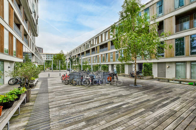 Велосипеды припаркованы возле забора во дворе между современными жилыми зданиями под голубым небом в дневное время — стоковое фото