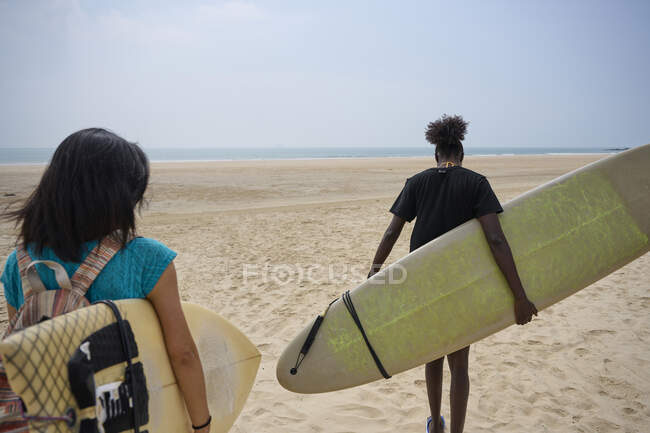 Back view of young multiethnic female surfers with surfboards speaking while strolling on sandy shore and looking and each other — Stock Photo