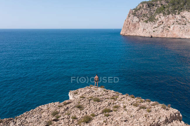 Вид с воздуха на неузнаваемый мужчина-путешественник, любующийся волнистым морем и скалой во время поездки на Ибицу, Испания — стоковое фото