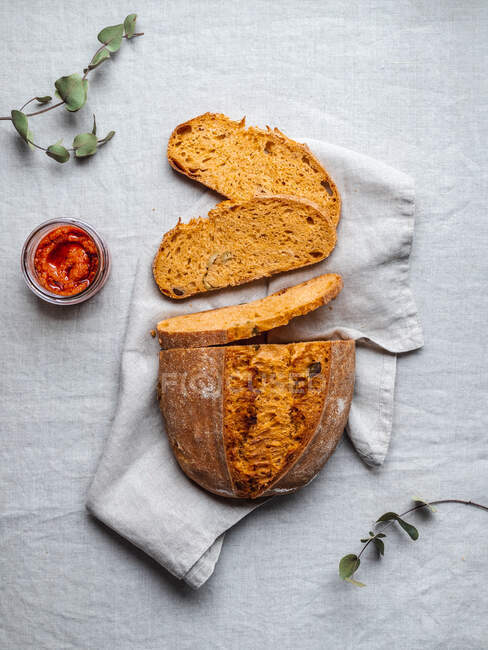 From above of loaf of bread and delicious Italian red pesto sauce arranged on napkin on table with plants — Stock Photo