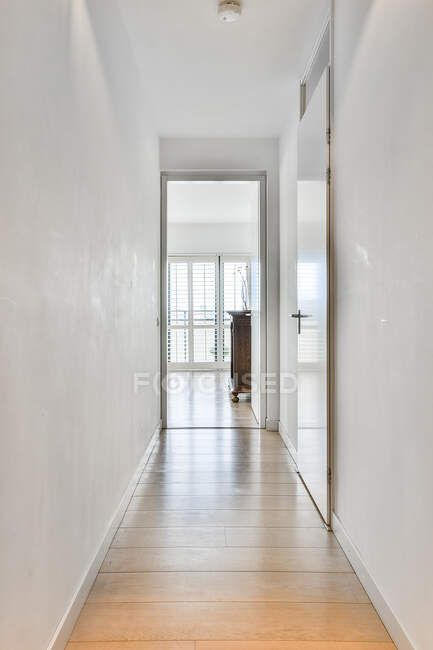 Stretto corridoio interno con pareti bianche e pavimento in legno sotto la lampada a casa durante il giorno — Foto stock
