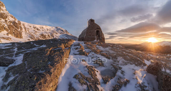 Espectacular paisaje de pequeña casa de piedra situada en la cima de la montaña nevada en la zona de las tierras altas en invierno al amanecer - foto de stock