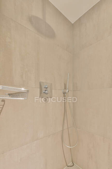 Interior del cuarto de baño con cabina de ducha con estante de metal y grifo en la pared de baldosas beige - foto de stock