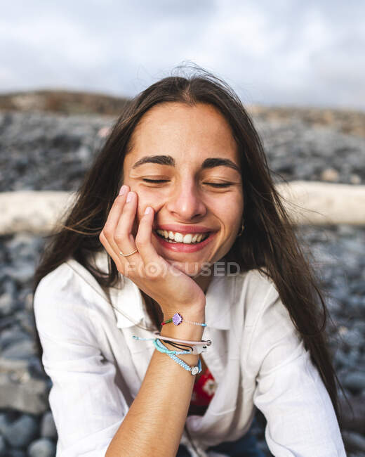 Adolescente feminina consciente com sorriso de dente e olhos fechados tocando o rosto enquanto descansa na praia em Tenerife Espanha — Fotografia de Stock