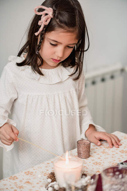 Menina bonito no vestido de pé perto da mesa festiva e velas relâmpago para celebrar as férias de Natal — Fotografia de Stock