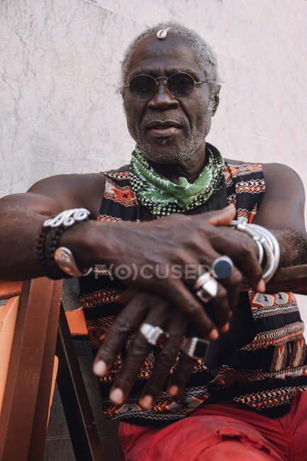 Cool middle aged African American male in rings and modern sunglasses sitting on chair in daylight — Stock Photo