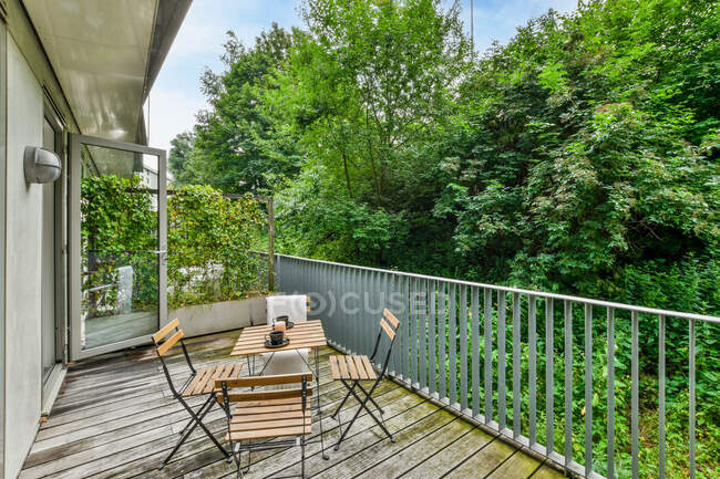 Kleiner Holztisch und Stühle auf der Terrasse vor grünen Bäumen am Tag — Stockfoto