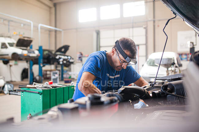 Vue latérale du technicien masculin mature occupé fixant le moteur de la voiture cassée dans une installation spacieuse de service de réparation — Photo de stock