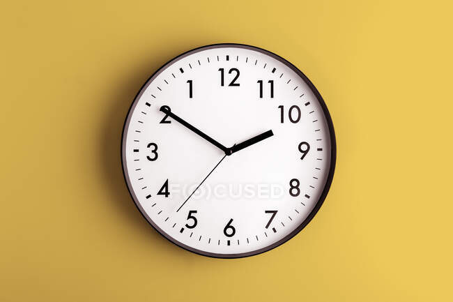 Reloj minimalista en forma redonda con números y flechas sobre fondo amarillo colorido - foto de stock