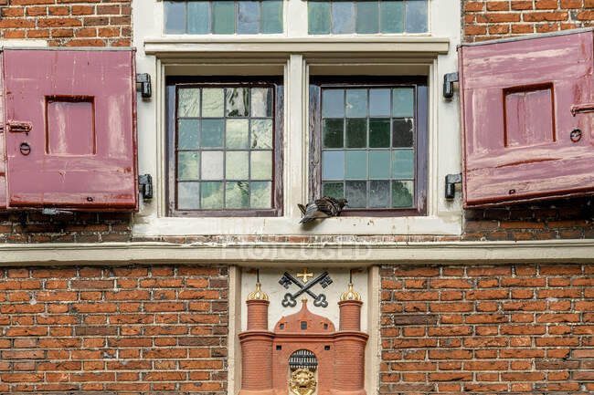 Exterior of medieval chantry with carved stone church in brick wall under bird on windowsill in Amsterdam Netherlands — Stock Photo