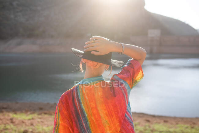 Rückansicht Frau blickt auf einen See mit einer Hand hält einen schwarzen Hut — Stockfoto