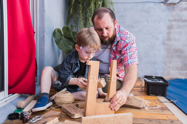 Focalisé papa barbu en chemise à carreaux avec garçon travaillant avec des blocs de bois — Photo de stock