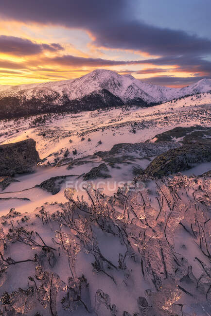 Paysage pittoresque de montagnes rocheuses couvertes de neige sous un ciel nuageux coloré au lever du soleil — Photo de stock