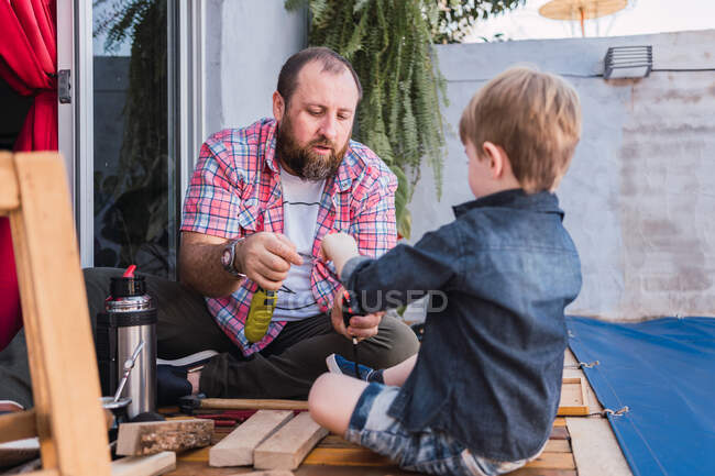 Unrasierter reifer Vater mit aufmerksamem Jungen, der Holzklötze mit Klebeband misst, während er Zeit auf verschwommenem Hintergrund verbringt — Stockfoto