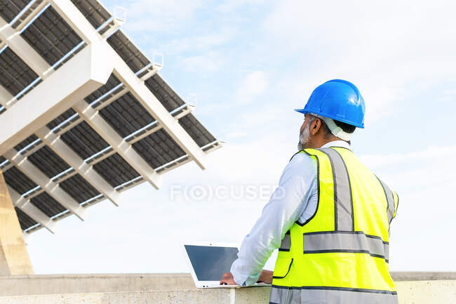 Supervisor masculino anônimo em uniforme trabalhando em netbook sentado perto da usina solar — Fotografia de Stock