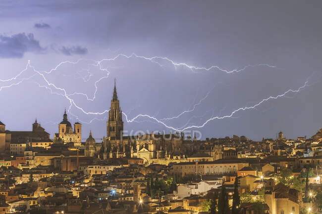 Paisaje urbano de Toledo con torre alta envejecida bajo cielo nublado con relámpagos durante tormenta en horario nocturno - foto de stock