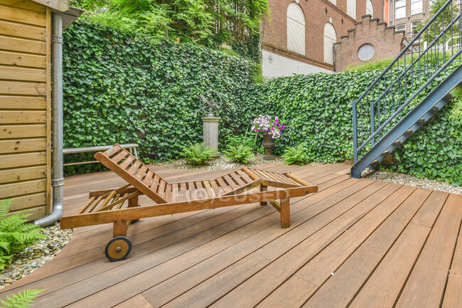 Bequemer Liegestuhl auf der Holzterrasse des Ferienhauses in der Nähe einer grünen Hecke im Sommer — Stockfoto