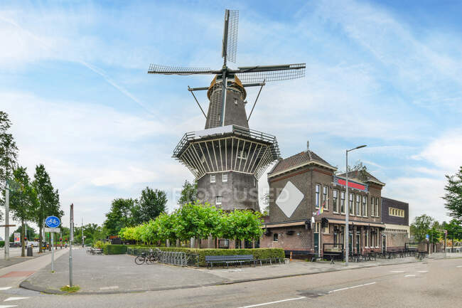 Gerador de vento envelhecido e casa de alvenaria exterior contra estrada de asfalto e árvores sob céu nublado em Amsterdam Holland — Fotografia de Stock