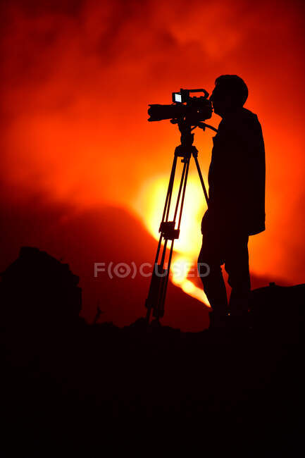 Vue latérale de la silhouette d'un homme enregistrant avec un trépied l'explosion de lave sur les îles Canaries de La Palma 2021 — Photo de stock