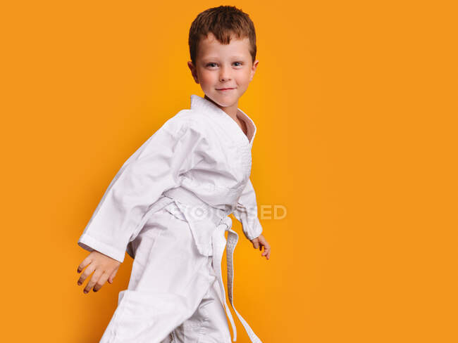 Vista lateral de um menino sorridente vestindo um quimono branco e olhando para a câmera — Fotografia de Stock