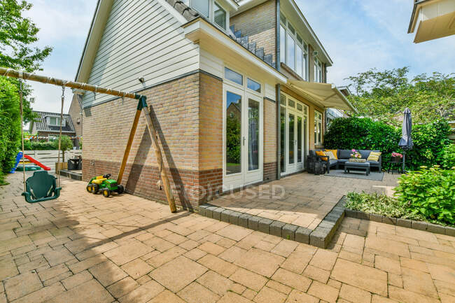 Giardino residenziale con altalena parco giochi in edificio in mattoni con piante verdi e pavimentazione — Foto stock