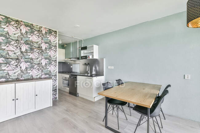 Интерьер современной кухни с деревянным обеденным столом и техникой в новой квартире — стоковое фото