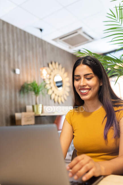 Souriant jeune entrepreneure assise à table et naviguant sur le netbook tout en travaillant sur un lieu de travail moderne — Photo de stock